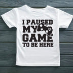 White t-shirt with black text and gaming controller graphic on a wooden surface