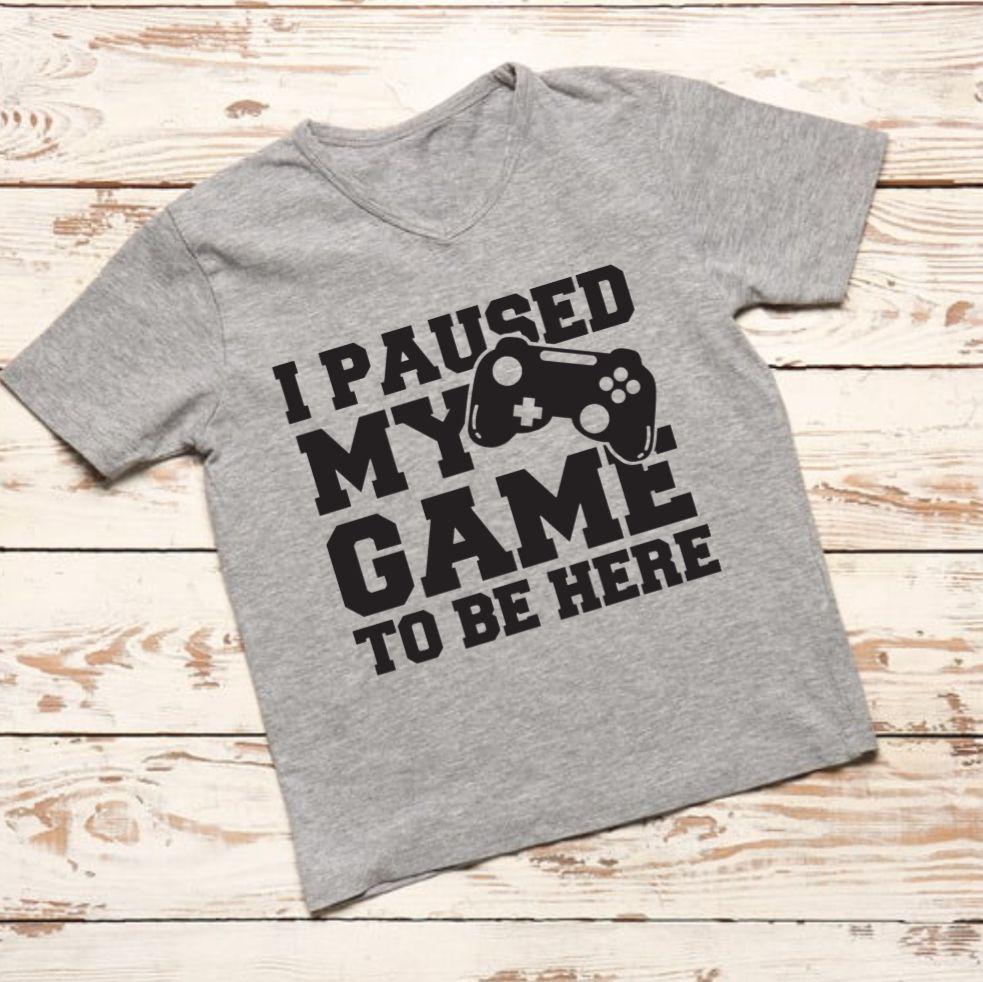 Gray t-shirt with 'I Paused My Game To Be Here' text on a wooden surface